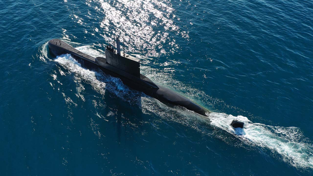 Aerial view of a submarine cruising on the surface of clear blue ocean water, creating white waves as it moves forward under bright sunlight, expertly engineered by the stress analysis team.