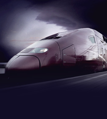 A sleek, dark-colored high-speed train speeds along a track. The background is dramatic, with stormy, dark clouds, creating a sense of movement and intensity. The train's design is modern and aerodynamic.